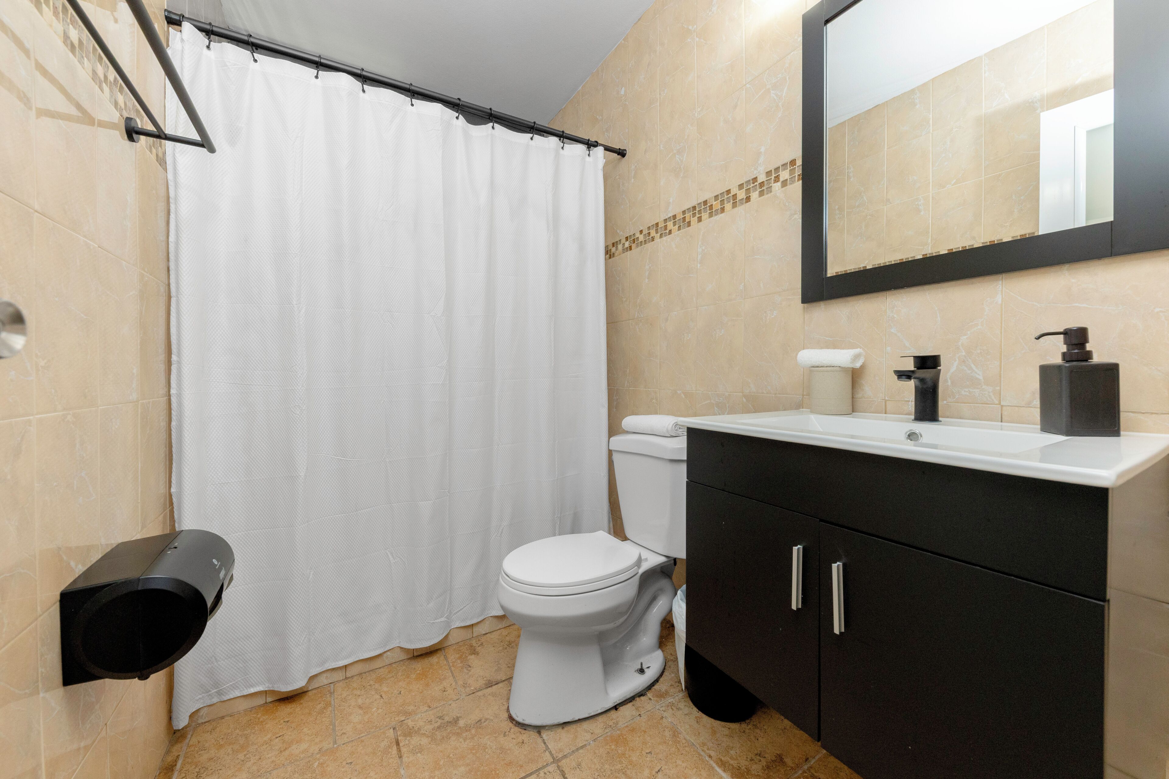 Une salle de bain équipée de toilettes, d’un lavabo, d’un miroir et d’un rideau de douche.