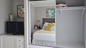 Un dormitorio con cama, televisor, cómoda y un cuadro en la pared.
