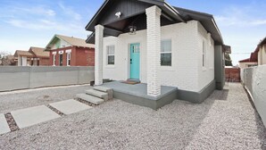 Et lille, etetages hus med facade af hvide mursten, en turkis dør og en overdækket veranda.