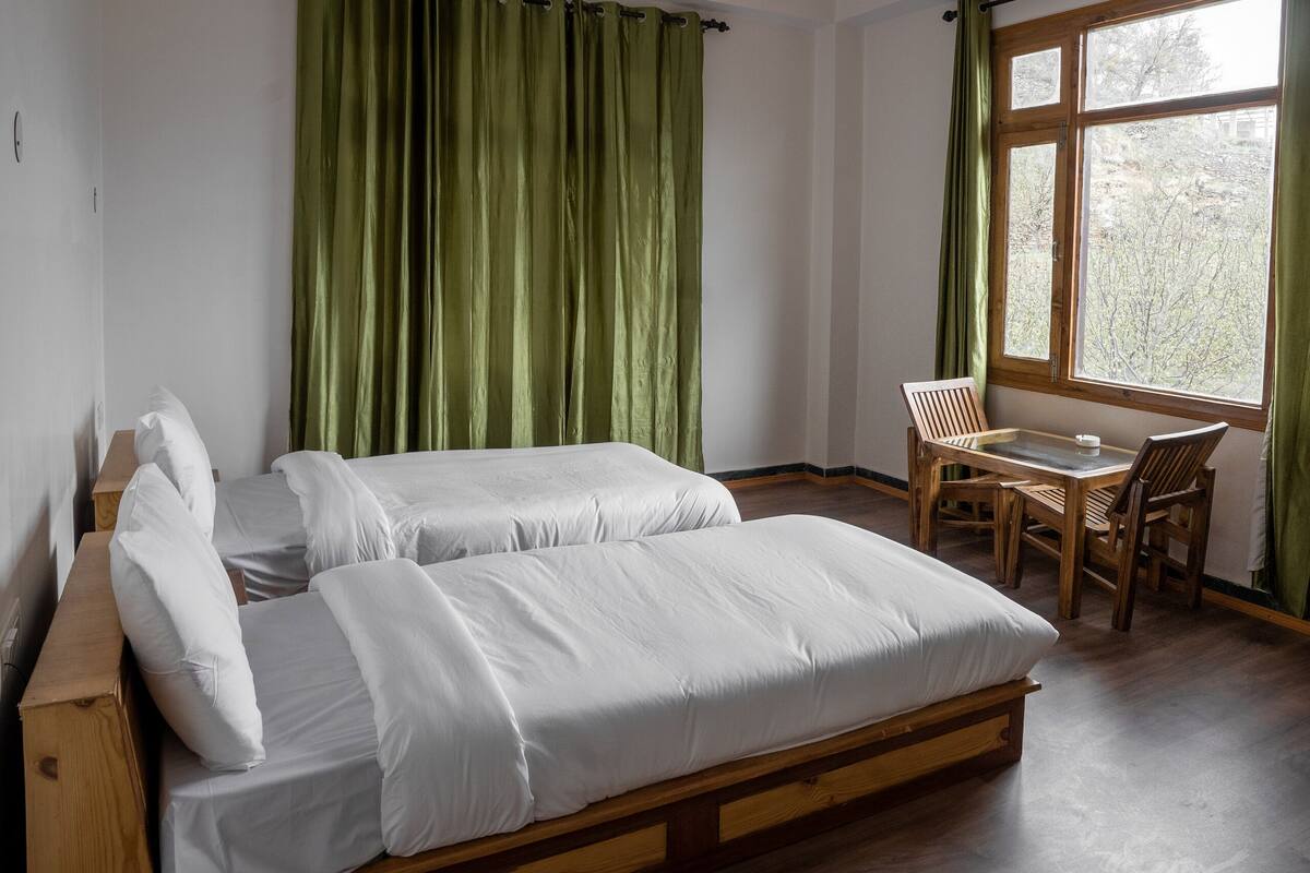 A room with a wooden bed, a small table, and a window with curtains.