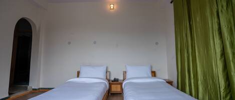 A room with two single beds, a small table, and a green curtain.