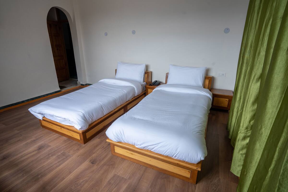 Two single beds with wooden frames and white bedding, a wooden floor, and a green curtain.