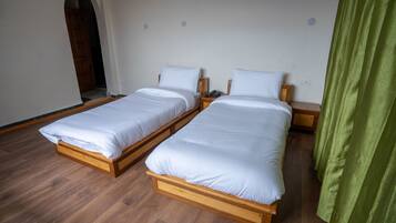 Two single beds with wooden frames and white bedding, a wooden floor, and a green curtain.