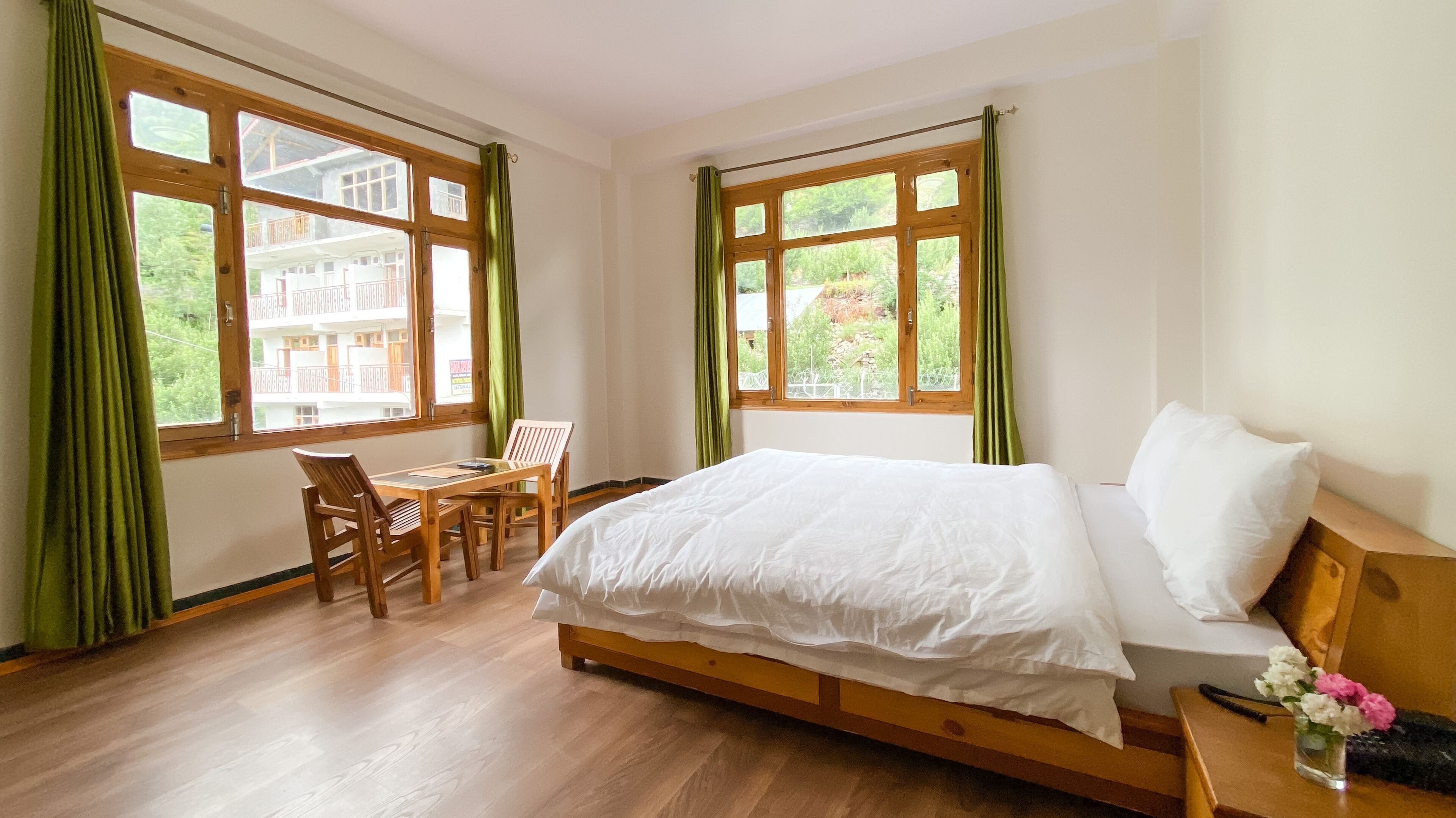 Un dormitorio con una cama de madera, un escritorio con sillas y ventanas grandes con cortinas.
