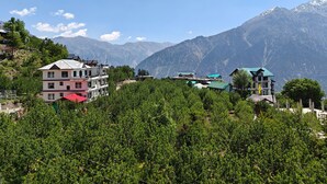 Un immeuble à plusieurs étages doté de balcons, entouré d’une végétation luxuriante et avec des montagnes en toile de fond.