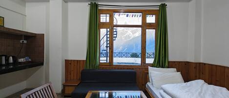 A cozy room with a wooden ceiling, a sofa, a bed, a glass-top table, and a window with curtains.