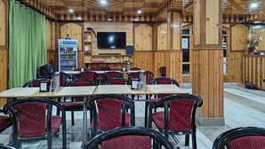 Un restaurant avec des murs lambrés, un téléviseur fixé au mur et des tables accompagnées de chaises rouges.