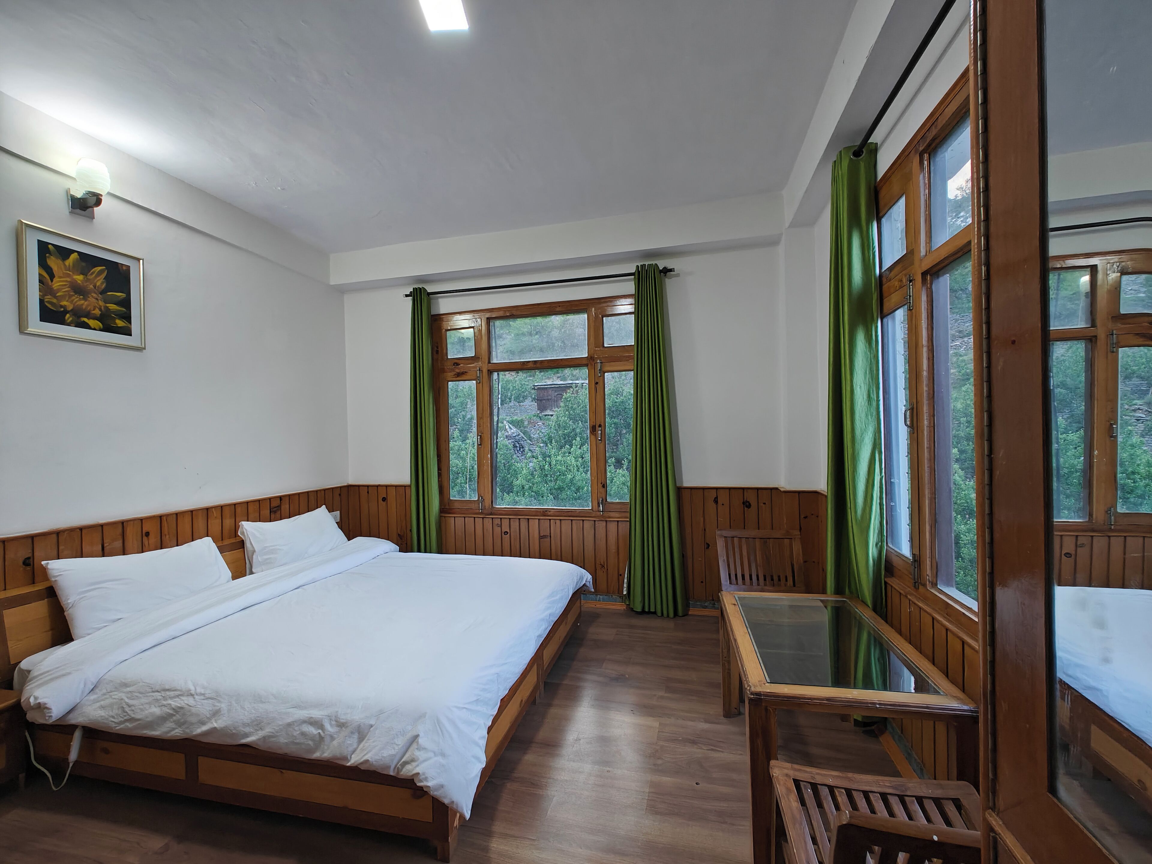 A bedroom with a wooden bed, a desk, and a window with green curtains.
