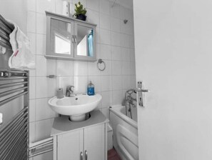 Bathroom features a sink, mirror, and toilet, with a shelf for personal items and a window above.