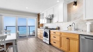 A modern kitchen with a view of the ocean, featuring wooden cabinets, stainless steel appliances, and a large window. - 2 bedroom Rio Del Mar Apt - Stunning Ocean Views (Aptos)