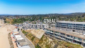 A coastal area with a modern building featuring multiple floors, a beach, and a hilly landscape in the background. - 2 bedroom Rio Del Mar Apt - Stunning Ocean Views (Aptos)