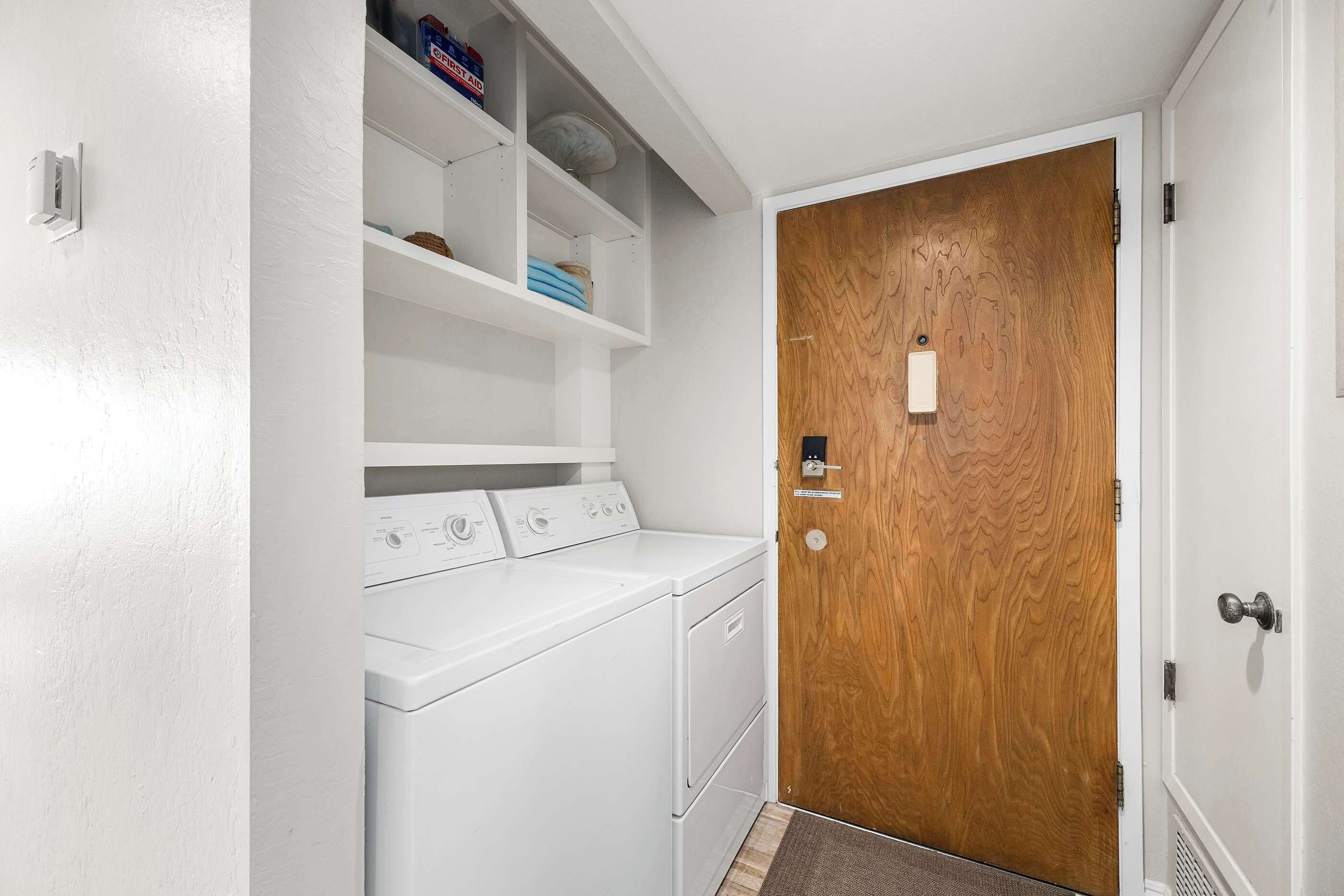 A laundry room with a wooden door, a white wall, and a shelf with folded towels.