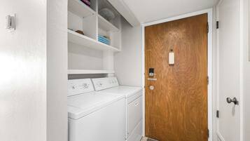 A laundry room with a wooden door, a white wall, and a shelf with folded towels.