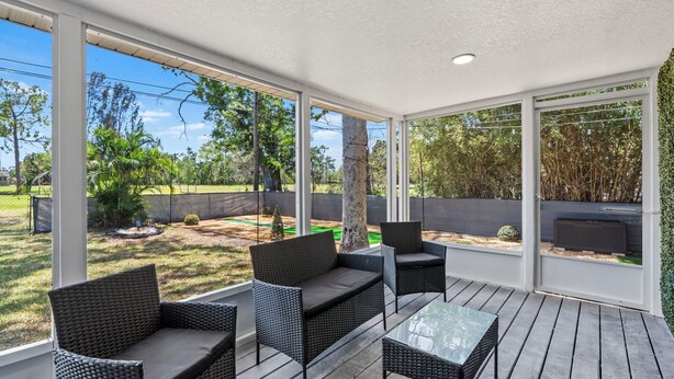 Un patio exterior con mobiliario de mimbre, ventanas amplias y vistas a un jardín paisajístico.