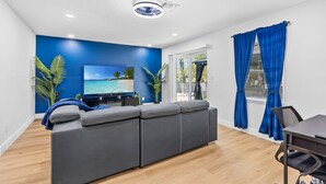 Una sala moderna con un sofá seccional gris, un televisor de pantalla plana y una pared de acento azul.