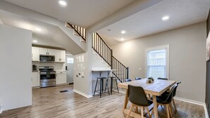 A spacious kitchen with modern appliances, a wooden dining table with chairs, and a staircase leading to an upper level. - Dundee Delight 3Br2Ba sleeps 9, central Omaha, heart of historical neighborhood (Omaha)