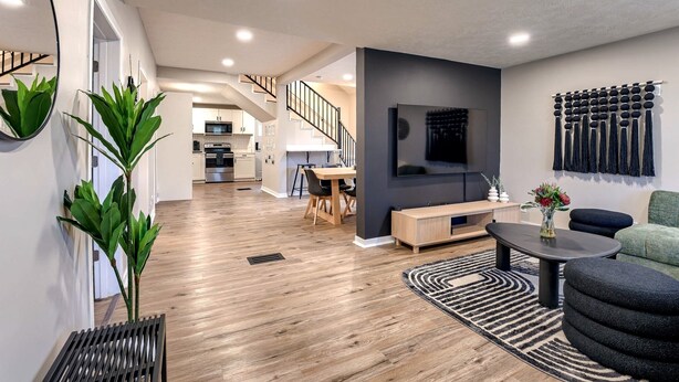 A modern living room with a wooden floor, a black sofa, a coffee table, and a TV mounted on the wall. - Dundee Delight 3Br2Ba sleeps 9, central Omaha, heart of historical neighborhood (Omaha)