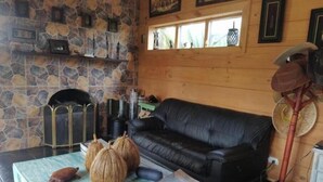 Un salon chaleureux avec un mur en pierre, un canapé en cuir noir, une table basse avec un livre et une lampe décorative.