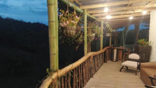 Une terrasse en bois avec une rambarde en bambou, une chaise et des plantes suspendues.