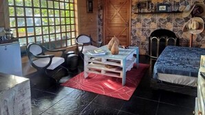 Une pièce chaleureuse avec un mur en pierre, une porte en bois, une cheminée, un lit, une table avec des chaises et une fenêtre donnant sur un paysage verdoyant.