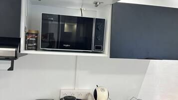 Cocina compacta con microondas, hervidor, tostadora y cafetera sobre una encimera de madera.