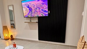 Una sala de estar moderna con un televisor de pantalla plana montado en la pared, una mesa redonda de centro con vasos y una botella, un tapete tejido y una planta en maceta.