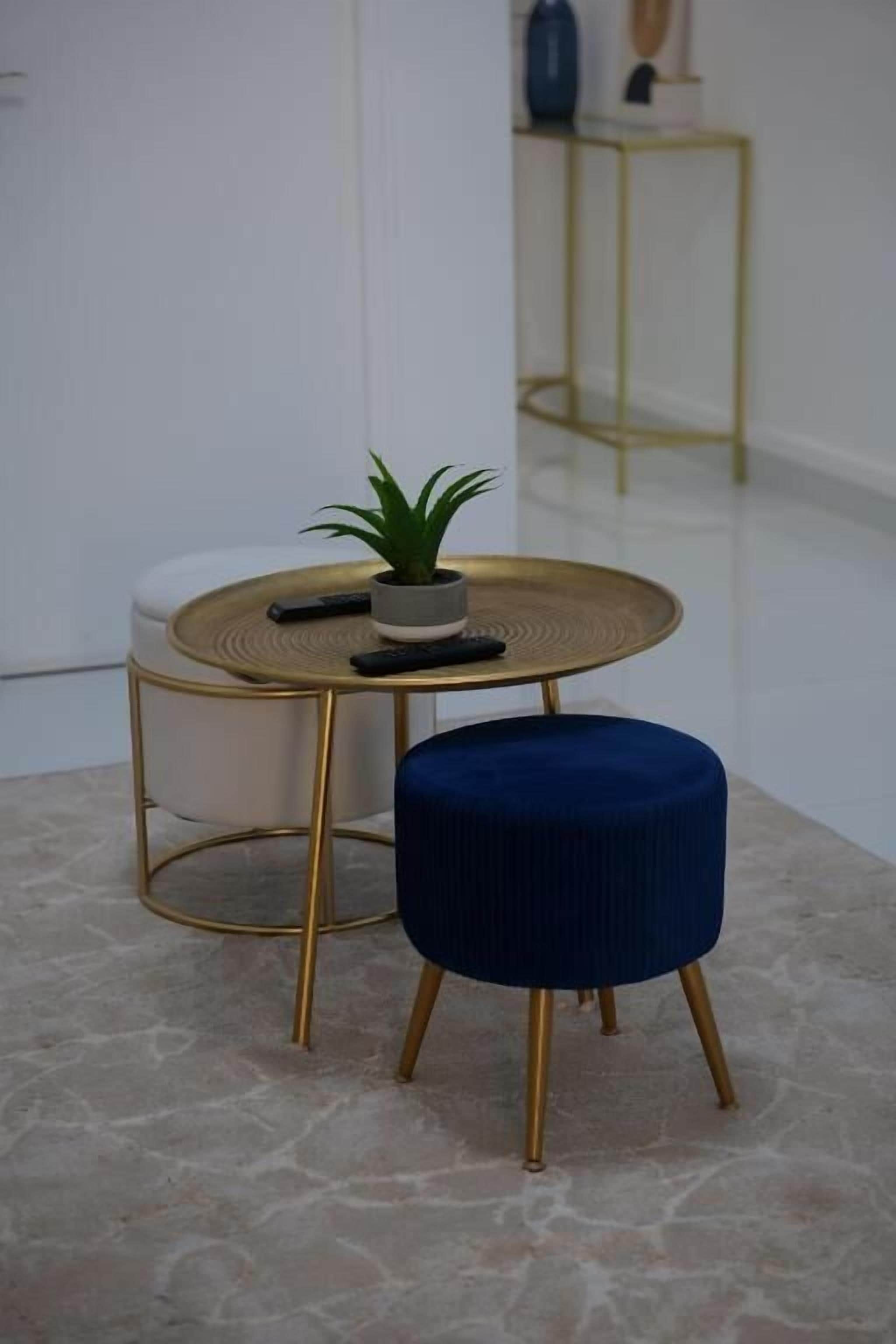 A modern room with a round gold table, a blue ottoman, and a small potted plant.
