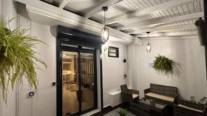 Un patio interior con puerta de cristal que da a un área de comedor, mobiliario de mimbre y plantas en macetas.