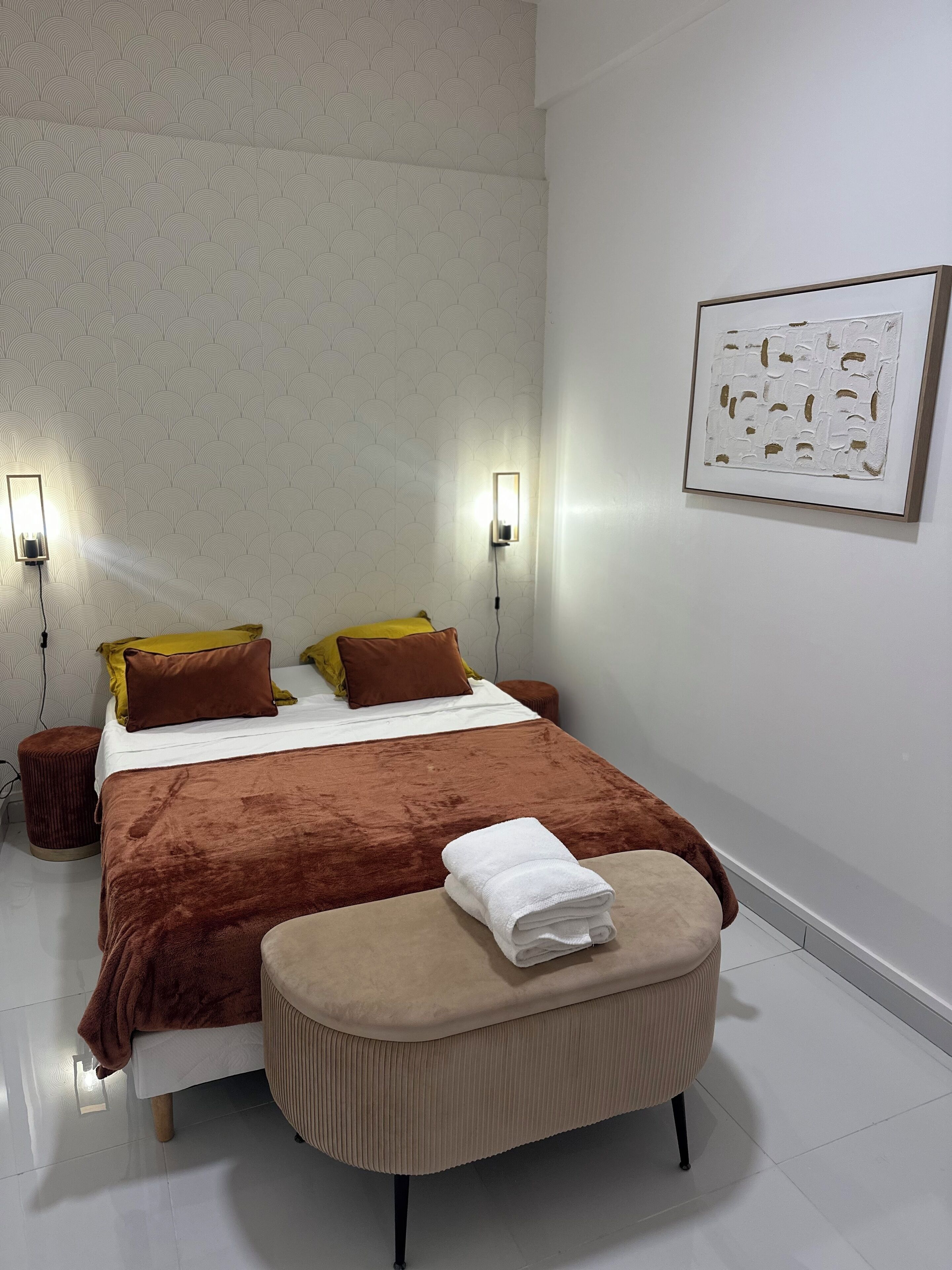 Ein ordentlich eingerichtetes Schlafzimmer mit einem großen Bett, zwei Nachttischlampen, einem gerahmten Kunstwerk an der Wand und einem kleinen Nachttisch.