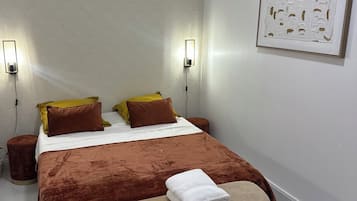 Ein ordentlich eingerichtetes Schlafzimmer mit einem großen Bett, zwei Nachttischlampen, einem gerahmten Kunstwerk an der Wand und einem kleinen Nachttisch.