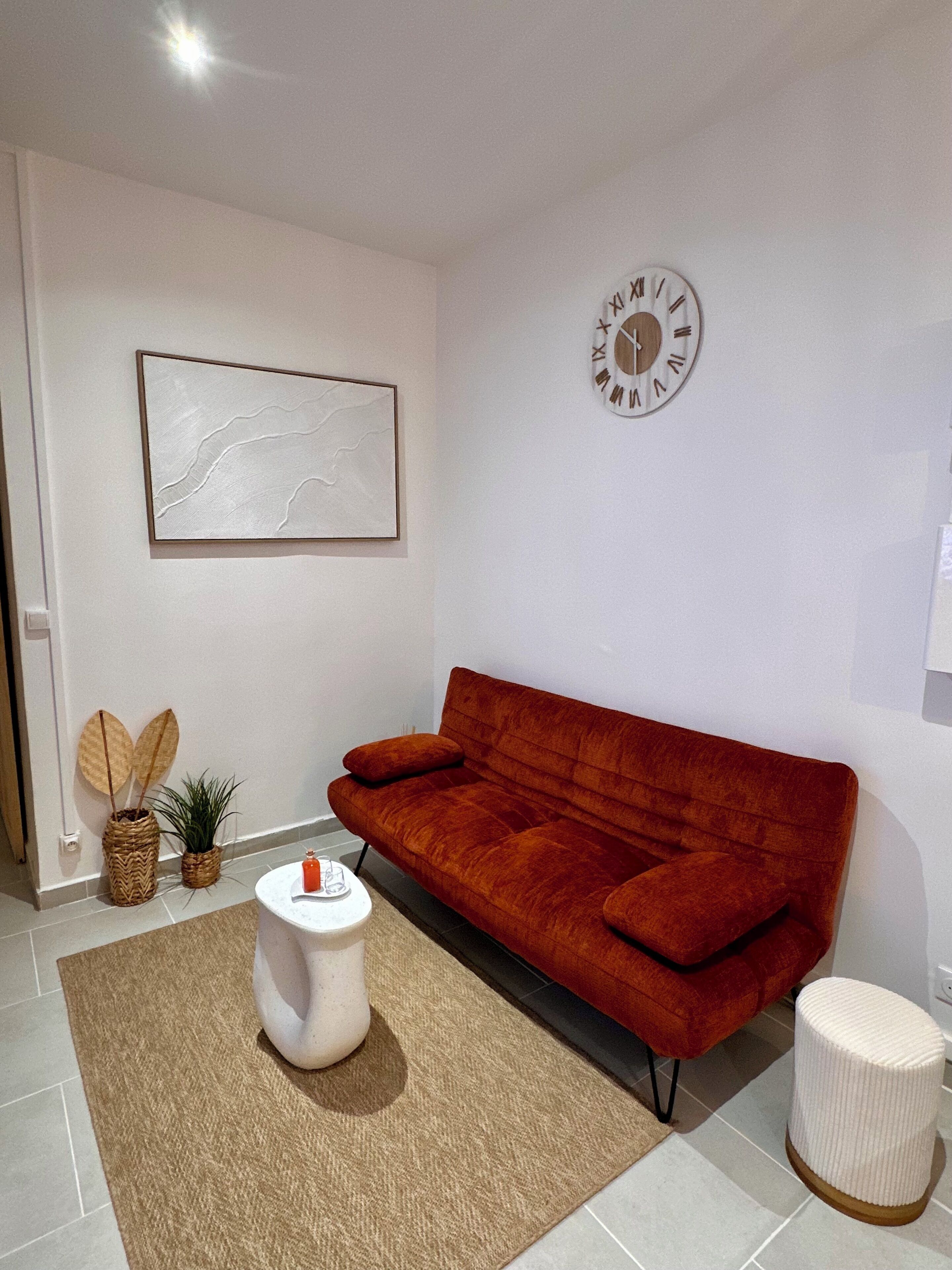 A modern living room with a red sofa, a round clock, a framed abstract painting, and two potted plants.