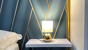 A bed with a white headboard, a bedside table with a lamp, and a wall with a geometric pattern.