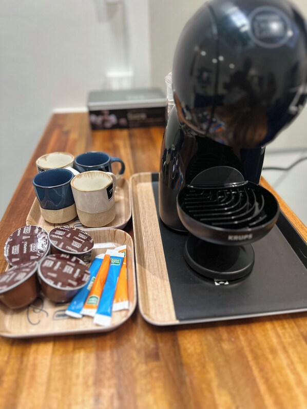 Una cafetera sobre una bandeja con tazas y un plato de bombones.