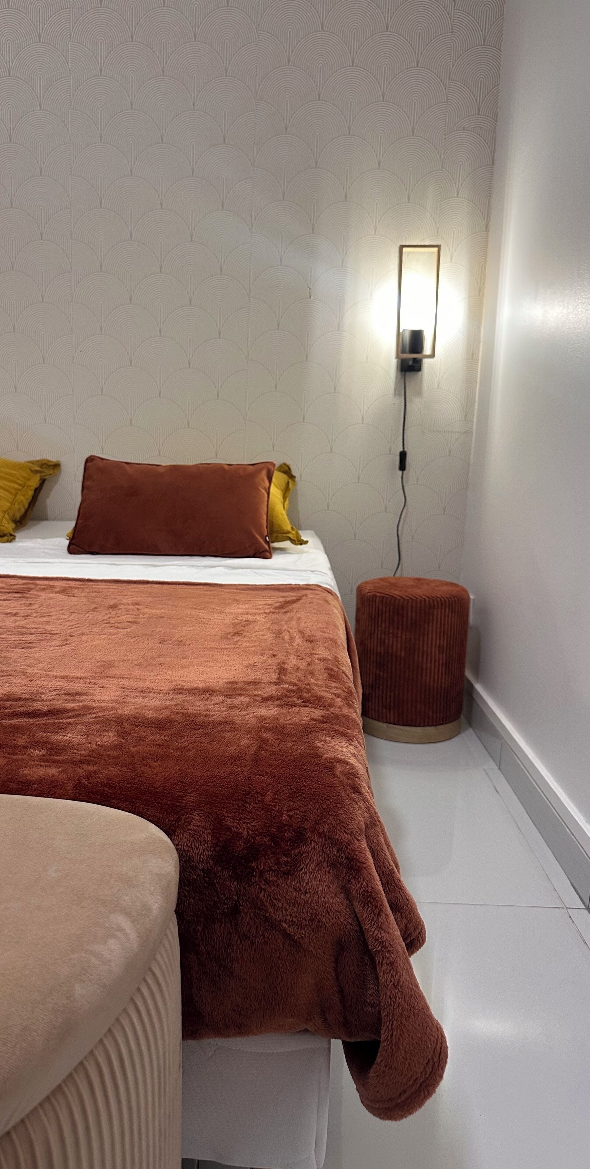 A bedroom with a bed, a nightstand, and a wall-mounted lamp.