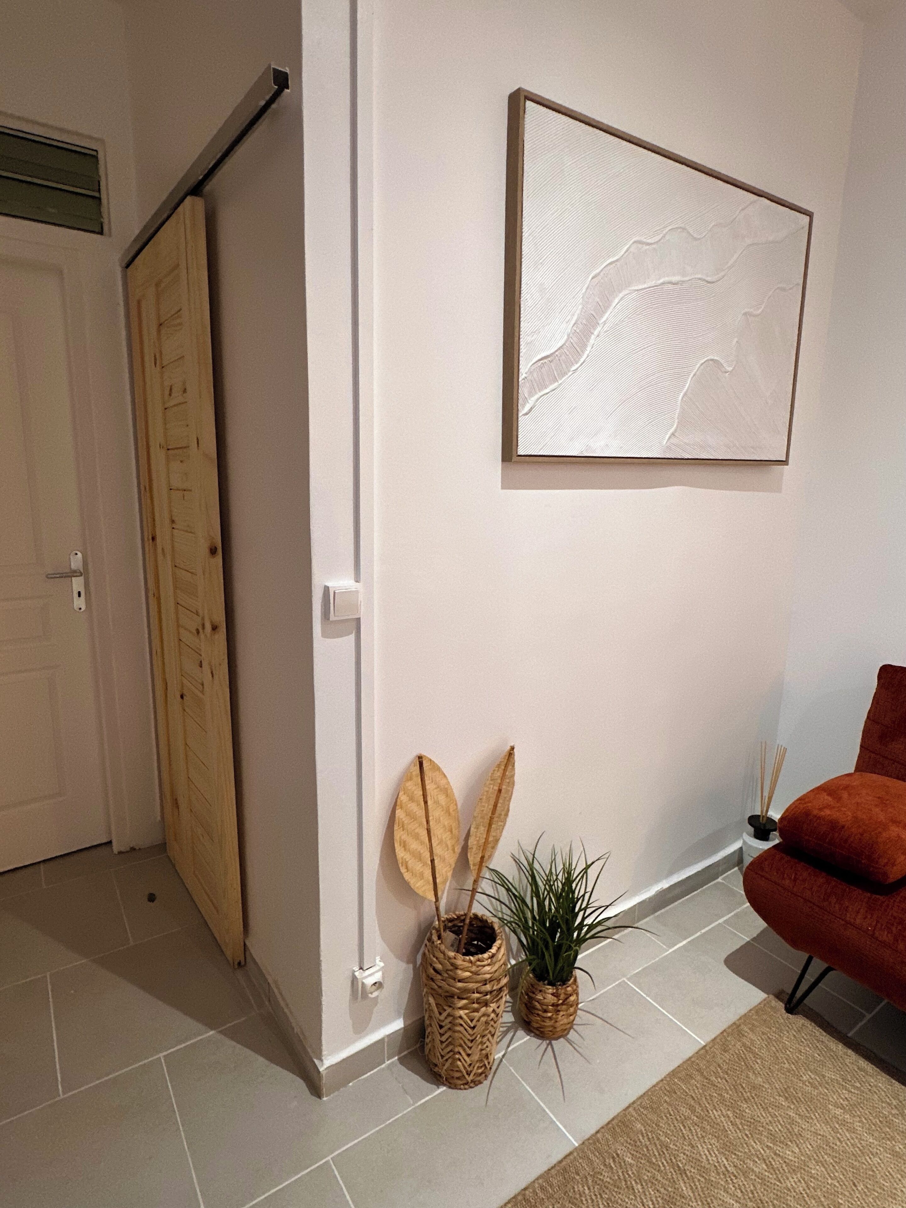 Une pièce avec une porte coulissante en bois, un tableau abstrait encadré, deux paniers en osier contenant des plantes et une chaise rouge.