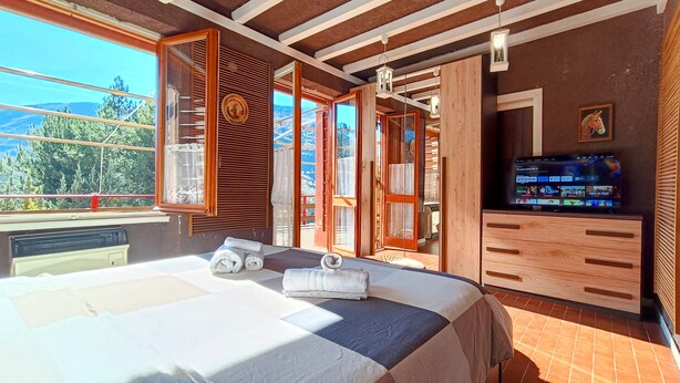 Ein Schlafzimmer mit Bett, Fernseher und Blick ins Freie.