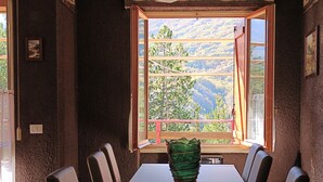 Ein Essbereich mit einem langen Tisch, Stühlen, einer Vase und einem Fenster mit Blick auf Bäume und Berge.
