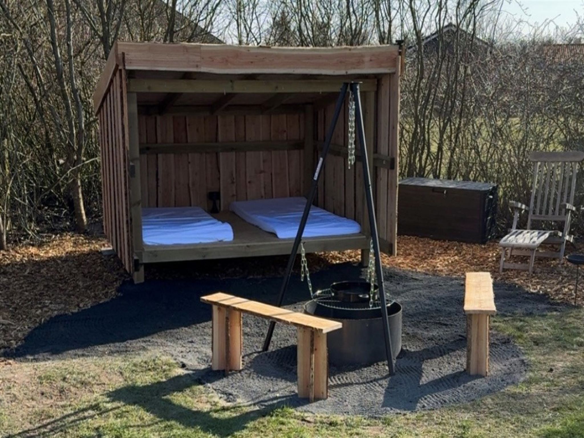 Une cabane en bois avec un lit, un banc et un foyer.