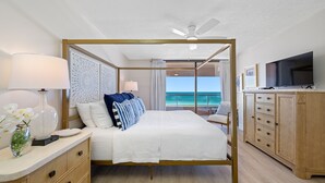 Una cama con dosel con vista al océano, un televisor y un minibar.