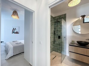 A modern bathroom with a glass shower enclosure, a round mirror, and a wooden vanity.