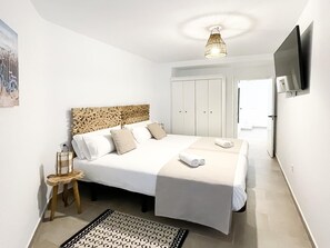 A bedroom with a bed, bedside table, lamp, and a TV on the wall.