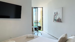 A modern hotel room with a bed, a flat-screen TV, a painting, and a view of the outdoors.