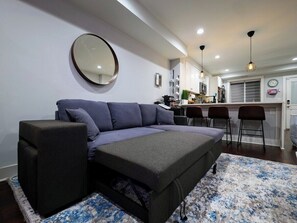 Ein modernes Wohnzimmer mit einer Couch, einem Couchtisch, einem runden Spiegel und einer Küchenzeile mit Barhocker.