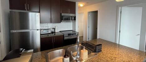 A modern kitchen with stainless steel appliances, granite countertops, and dark wooden cabinets.