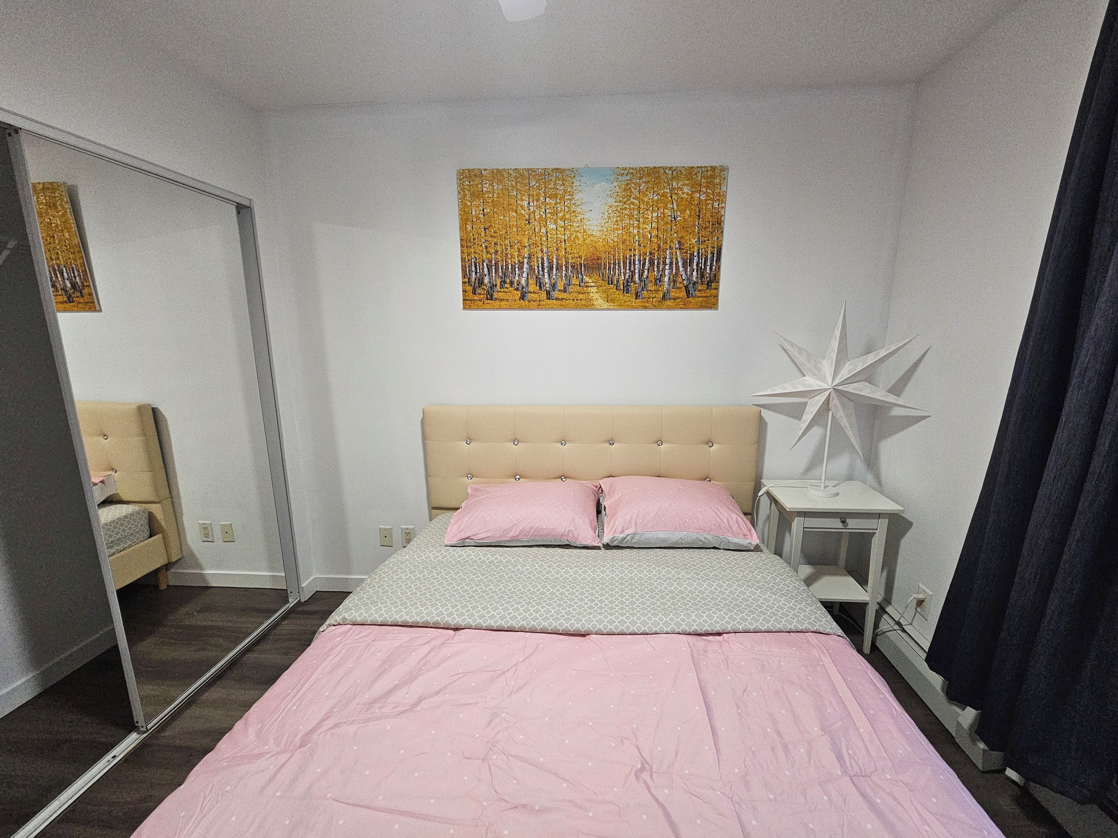 Ein Schlafzimmer mit einem Bett, einem Nachttisch, einer sternförmigen Lampe, einem Bild an der Wand und einer Tür zu einem anderen Raum.