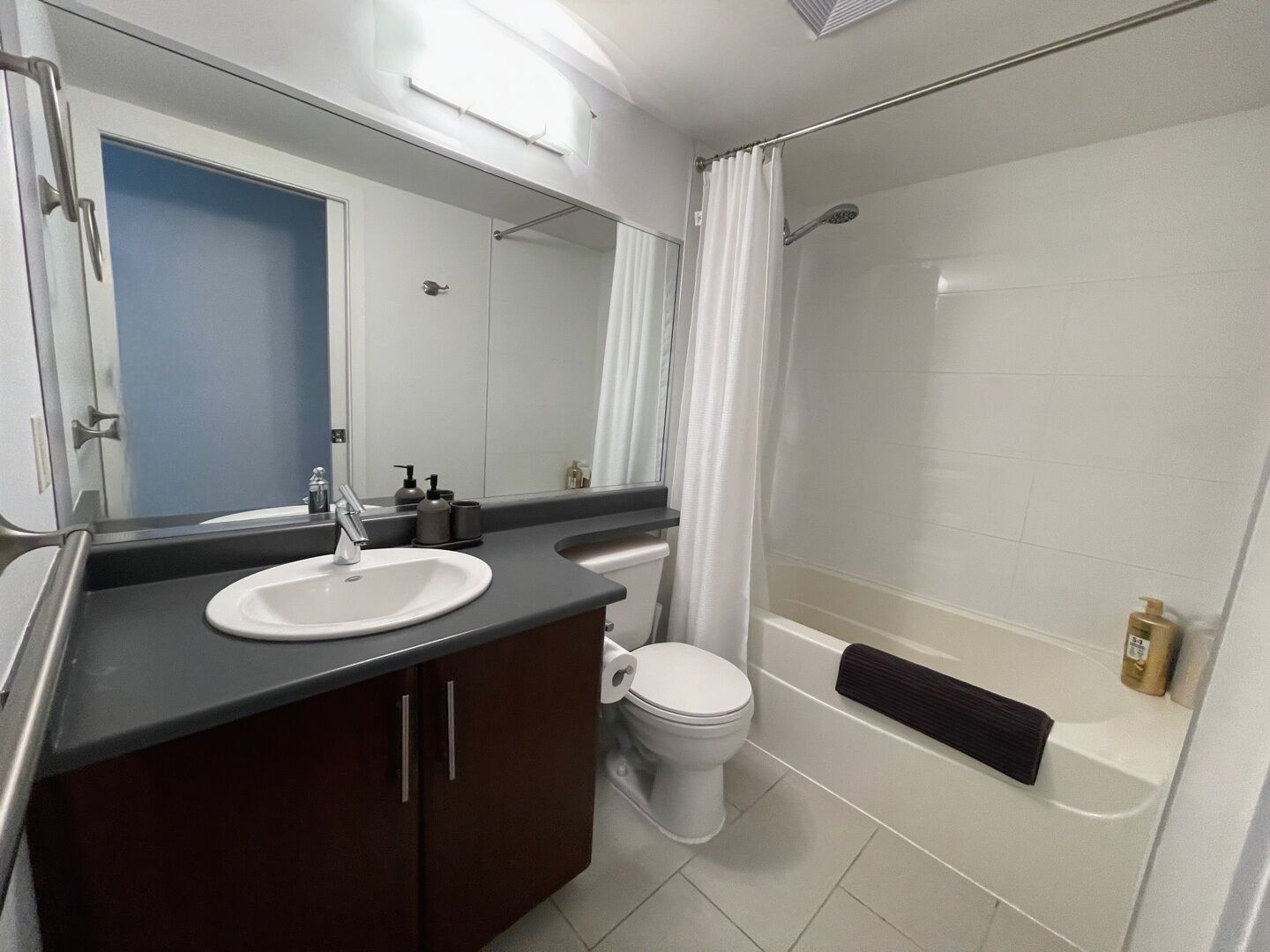 Ein modernes Badezimmer mit Waschbecken, dunklem Holzschrank, Toilette und Duschbereich.