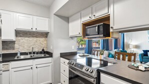 A modern kitchen with white cabinets, a microwave, a stove, and a sink.