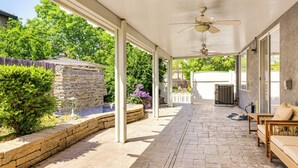 Eine überdachte Terrasse mit Deckenventilator, Steinwand und Backsteinboden.