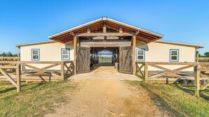 A stable with a wooden roof and open entrance, surrounded by a dirt path and wooden fences.