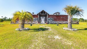 A rustic barn-style building with a front porch, surrounded by a well-maintained lawn and palm trees.